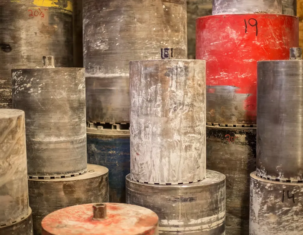 Several large, weathered metal cylinders are stacked closely together, with one red cylinder marked "19" among mostly gray ones—typical equipment used in concrete cutting services Hamilton.