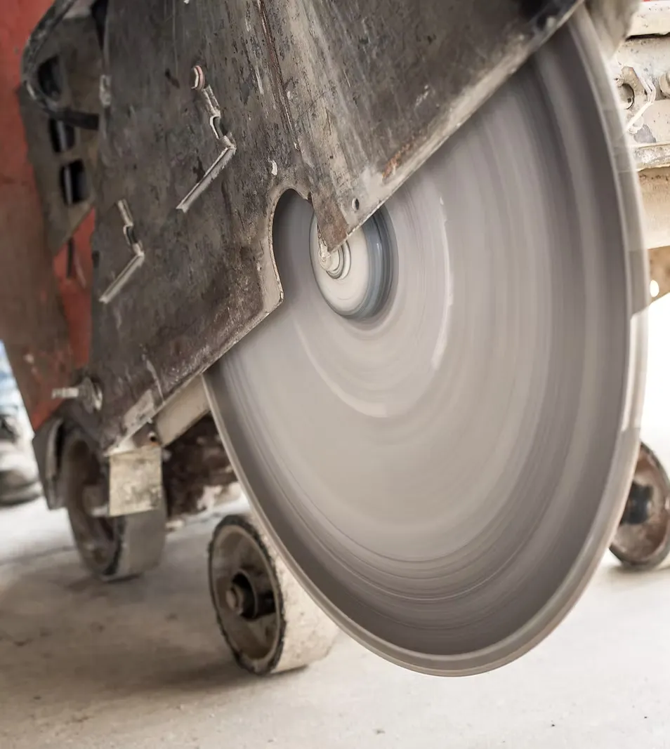 Close-up of a large, spinning circular saw blade cutting through concrete, expertly maneuvered by a concrete contractor using a wheeled cutting machine.