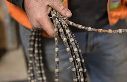 A concrete contractor's hand holds several segments of worn, striped wire or cable, with a close-up focus on the hand and the cables.